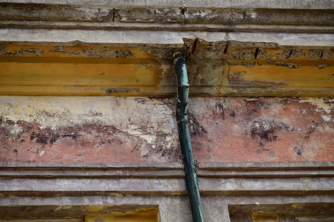 Détail d'un mur ancien avec un conduit en métal, montrant des signes d'usure et de dégradation.