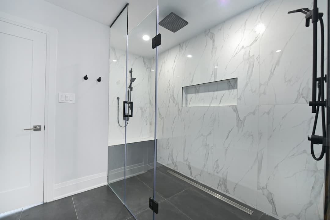 Salle de bain moderne avec douche en verre et carrelage marbré, éclairage LED.